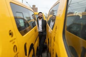 Zohran Mamdani standing in the middle of a fleet of NYC taxis.